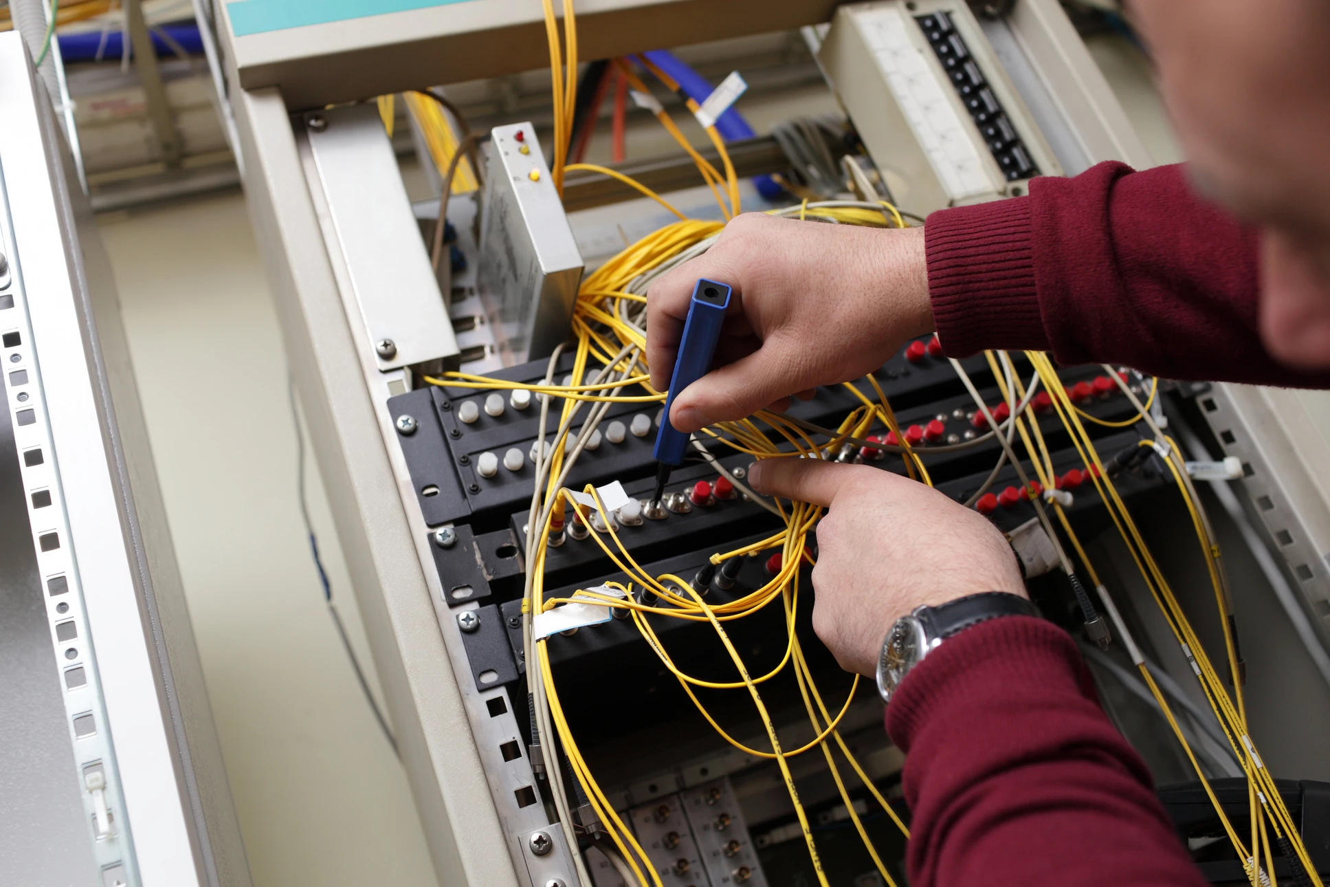 Technicien en pull bordeaux travaillant sur équipement de télécommunications dans baie de brassage