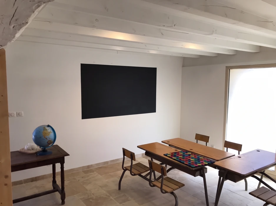 Salle de classe rénovée, style épuré, murs blancs, plafond avec poutres apparentes peintes en blanc