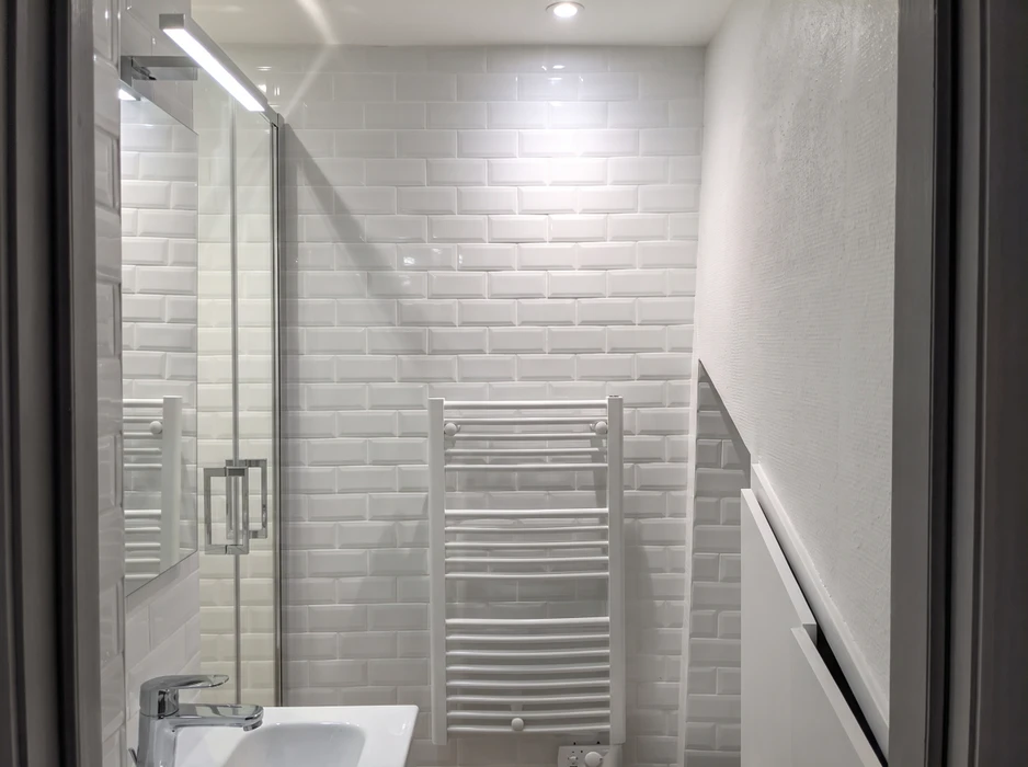 Salle de bain moderne avec carrelage métro blanc brillant en brickwork, radiateur sèche-serviettes chromé tubulaire incurvé mural, paroi de douche en verre trempé avec profilé aluminium anodisé