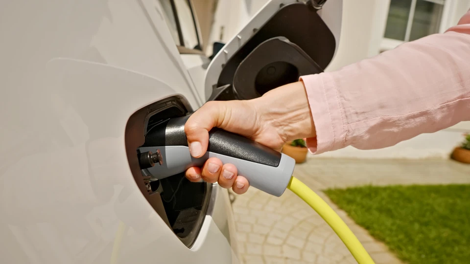 Borne de recharge pour véhicule électrique installée en extérieur sur mur en crépi jaune, près d'un garage
