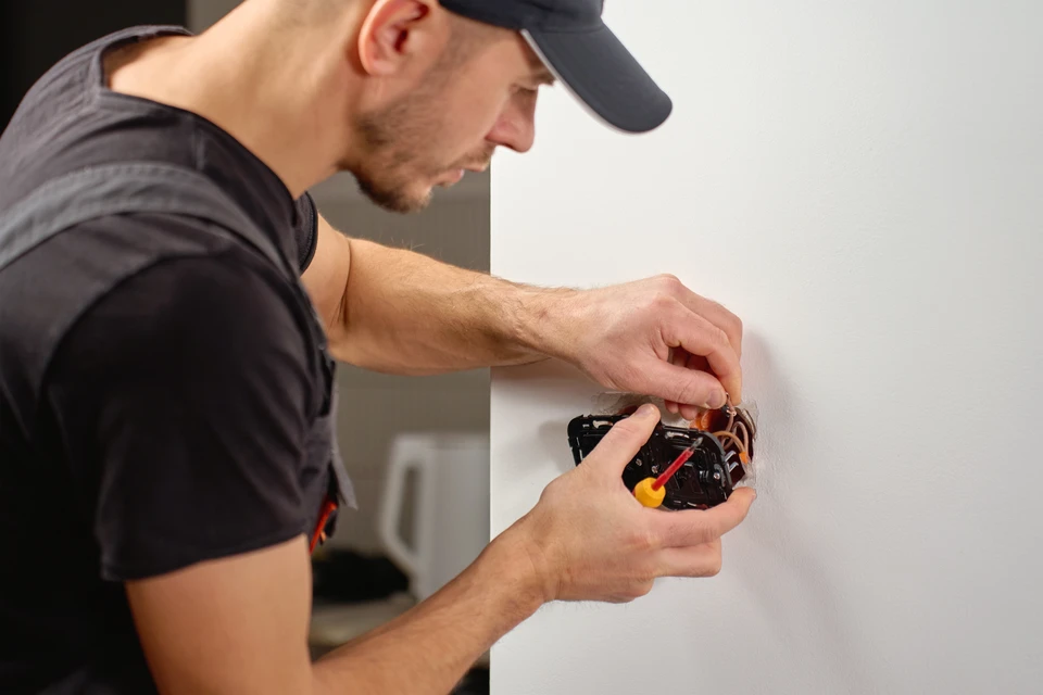 Électricien en combinaison de protection travaillant sur un tableau électrique industriel, utilisant un multimètre pour effectuer des mesures de contrôle et diagnostic