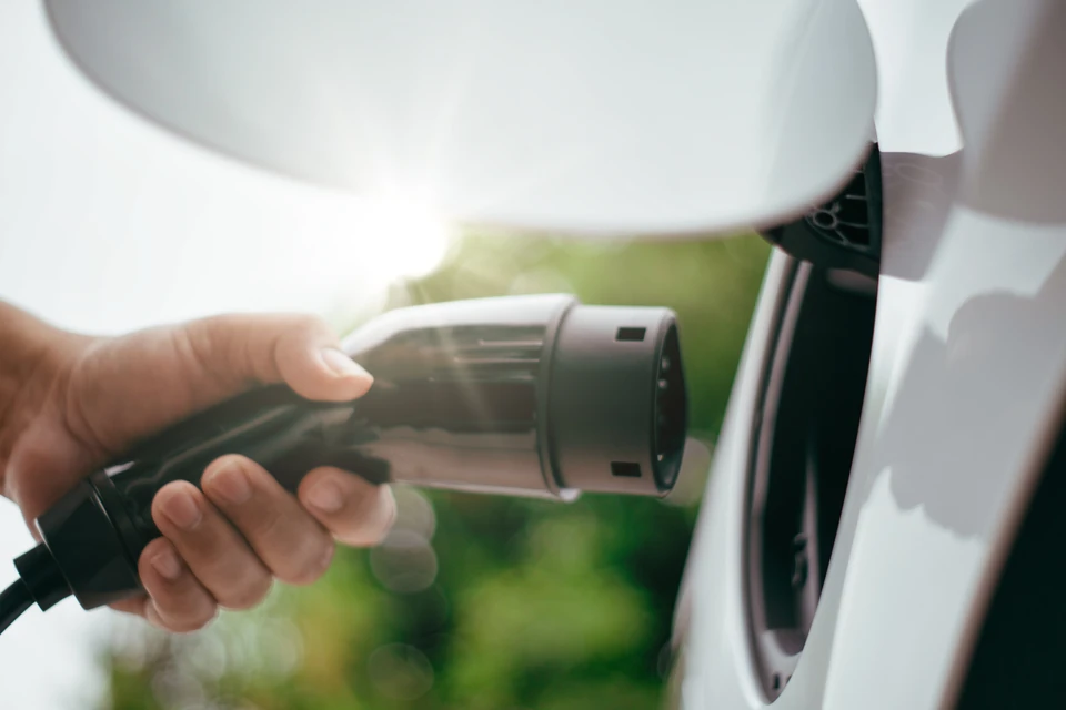 Électricien qualifié raccordant les câbles électriques à l'intérieur d'une borne de recharge murale blanche Type 2 fixée sur un mur extérieur résidentiel en crépi clair. Boîtier ouvert révélant le câblage, connecteurs et bornes électriques. Professionnel en tenue de travail, tournevis à la main, gros plan sur l'installation des connexions. Borne neuve, état de neuf, installations conformes.